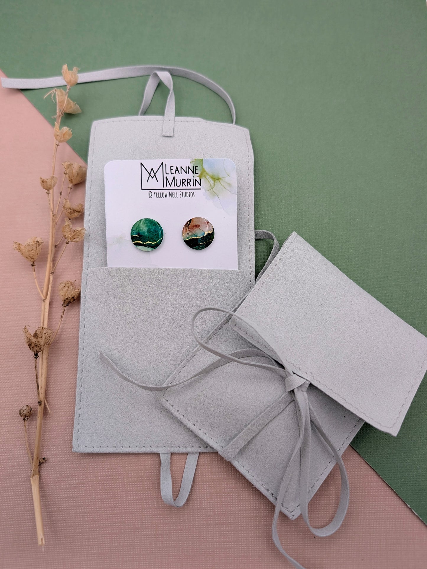 Gray jewelry pouch with earrings and a card on a green background