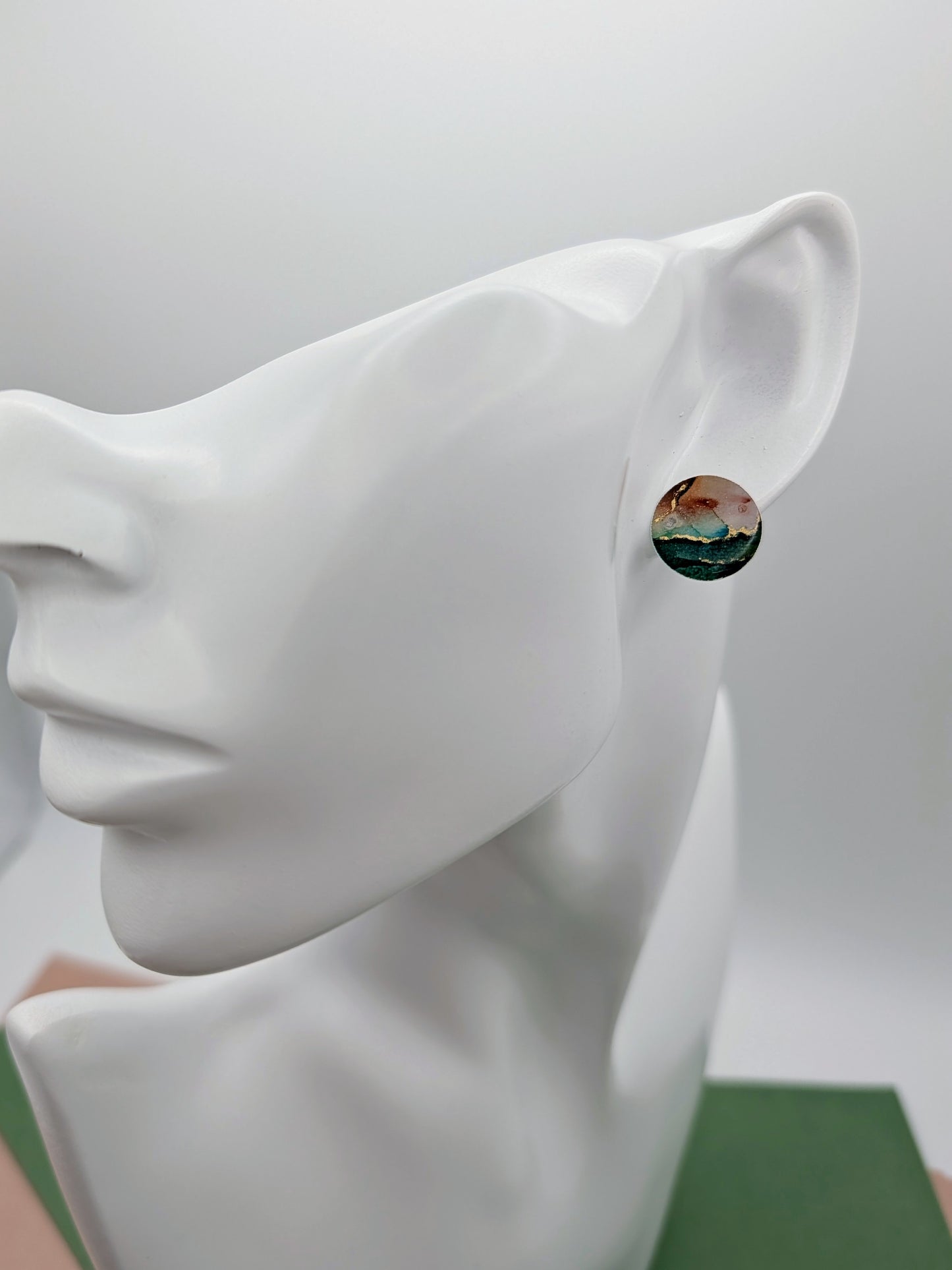 Round earrings with a scenic design on a white mannequin ear