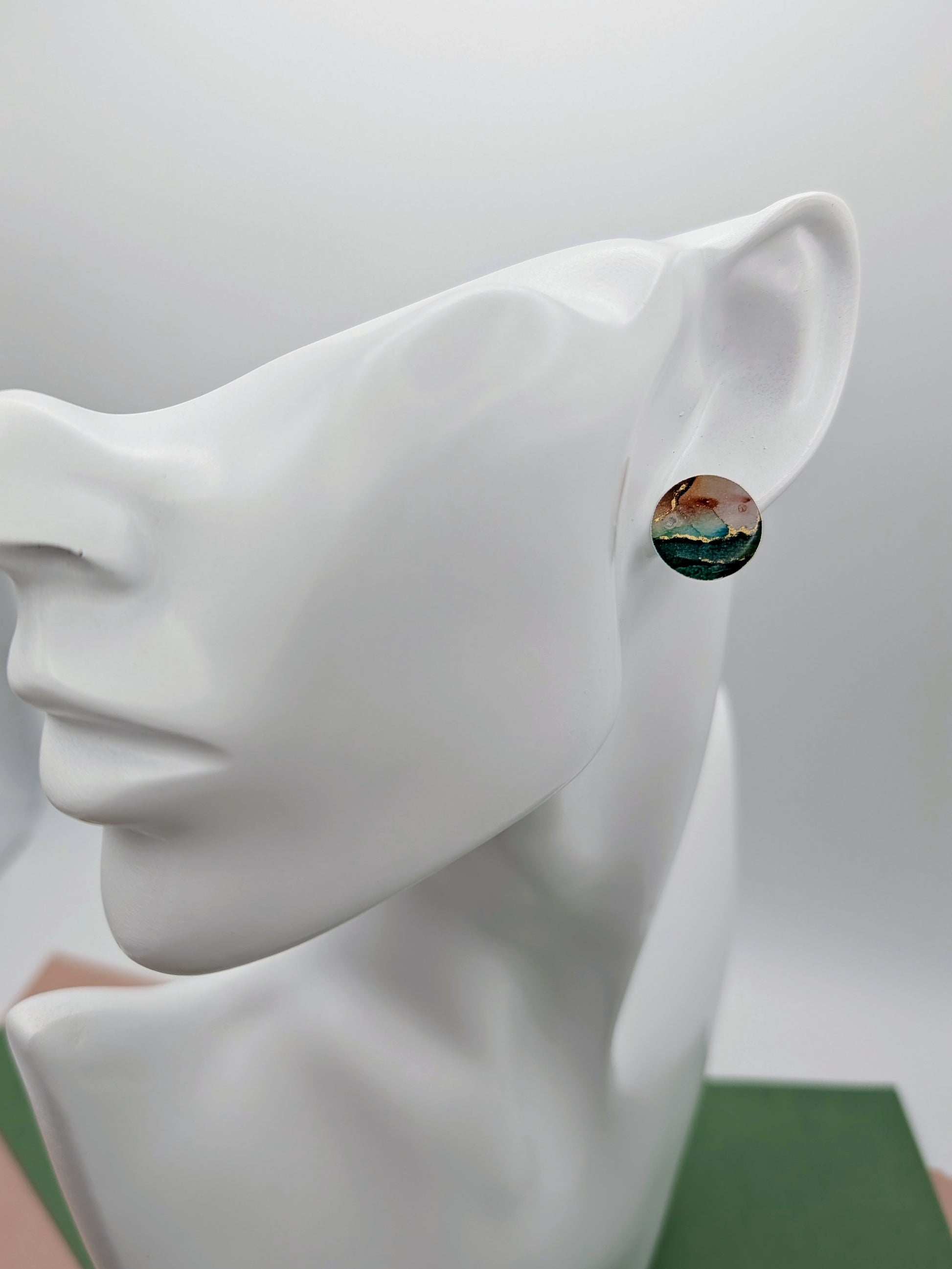 Round earrings with a scenic design on a white mannequin ear