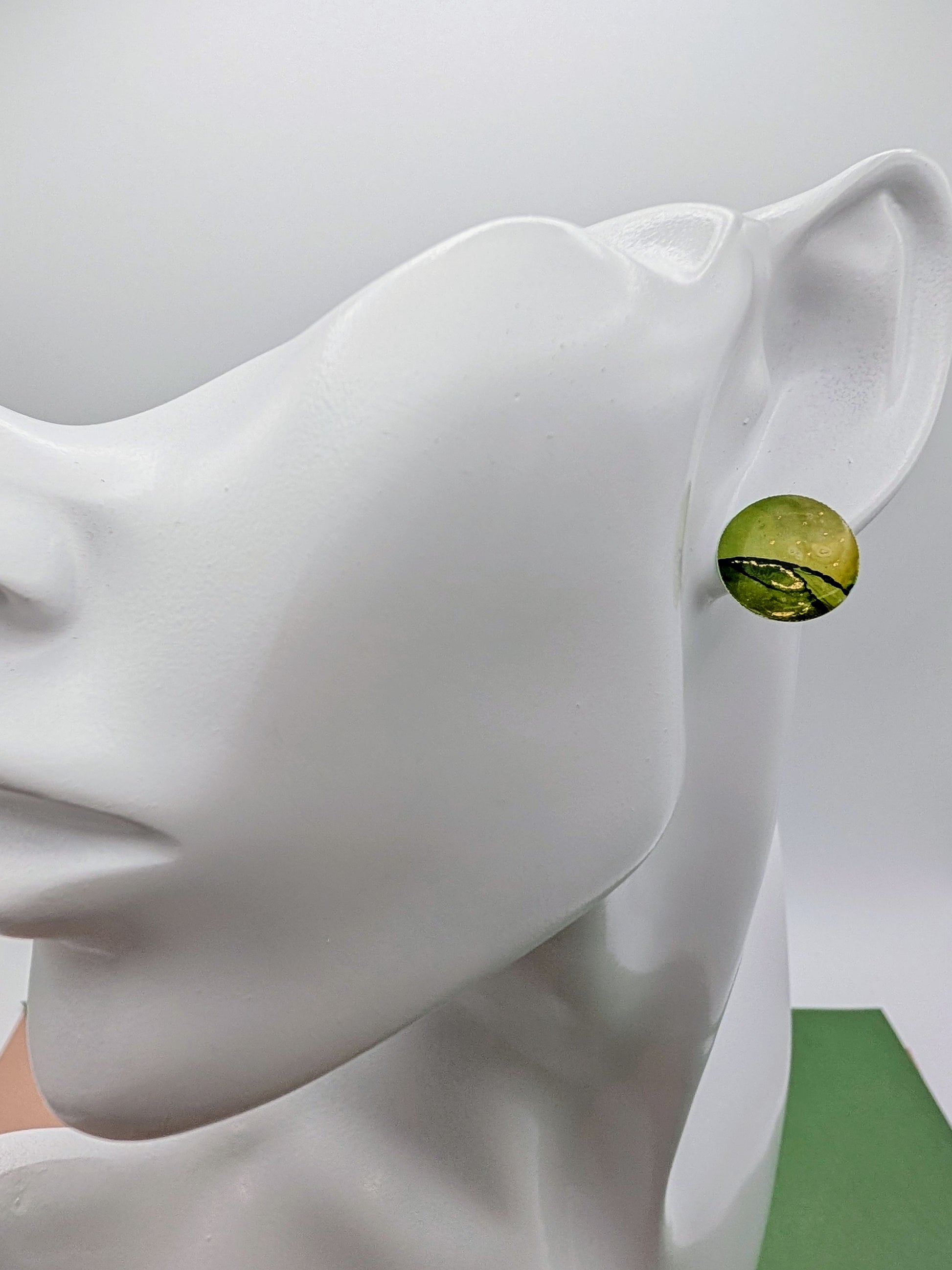 Green earring on a mannequin ear against a gray background